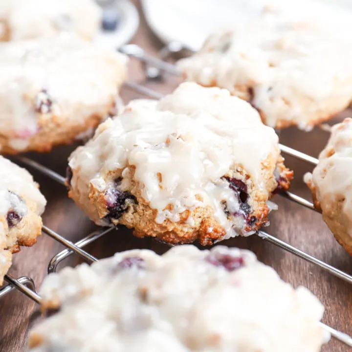 Up close side view of a baked blueberry fritter on a cooling rack surrounded by other fritters.