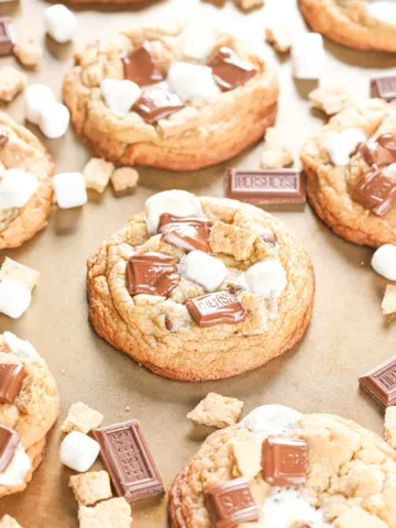 Edge view of a bakery style smores cookie on a baking sheet surrounded by the rest of the batch of cookies.