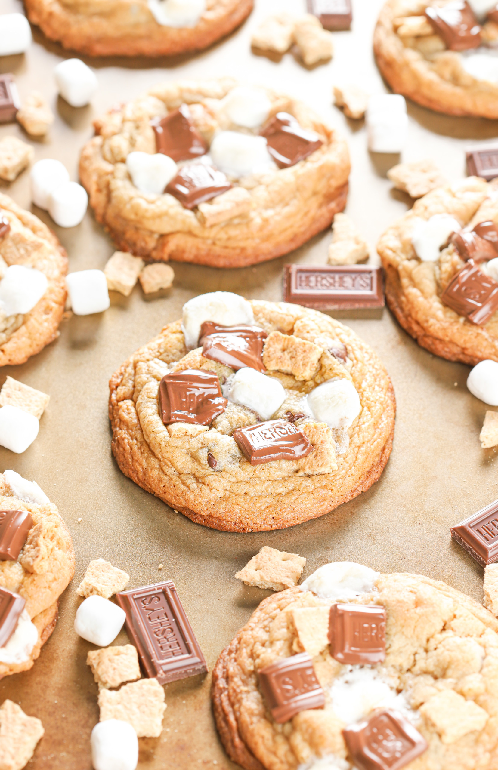 Edge view of a bakery style smores cookie on a baking sheet surrounded by the rest of the batch of cookies.
