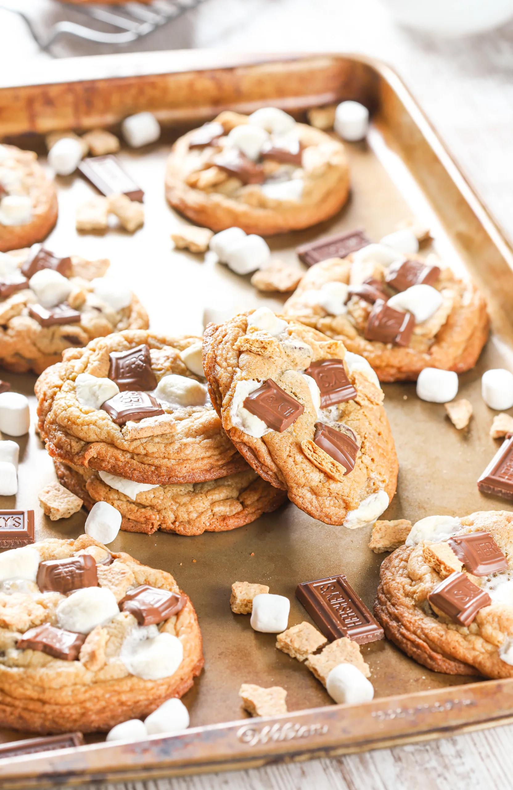 A stack of smores cookies on a cookie sheet with the remainder of the batch of cookies surrounding the stack.