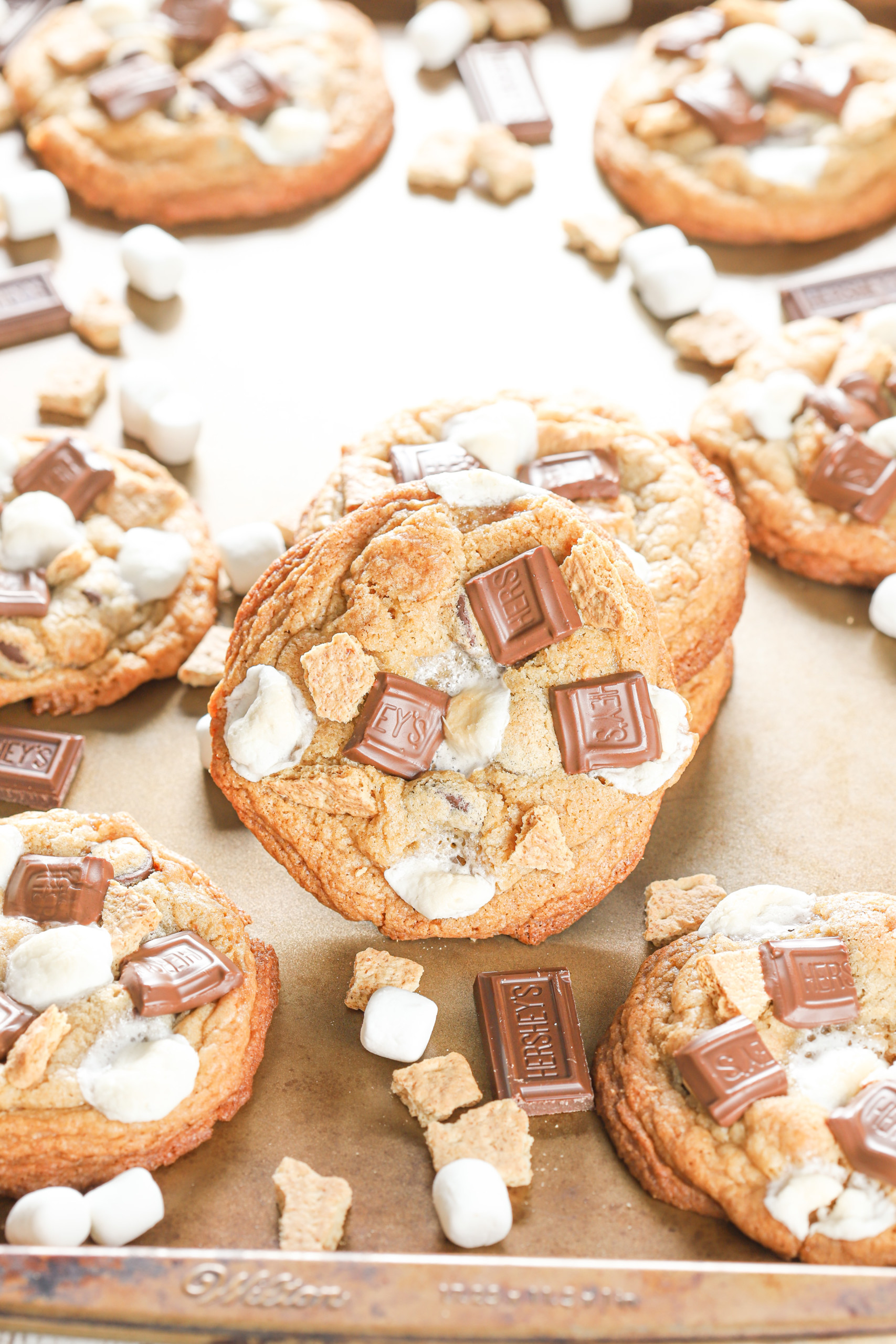 Up close side view of a chewy smores cookie leaning against a stack of smores cookies on an aluminum baking sheet.