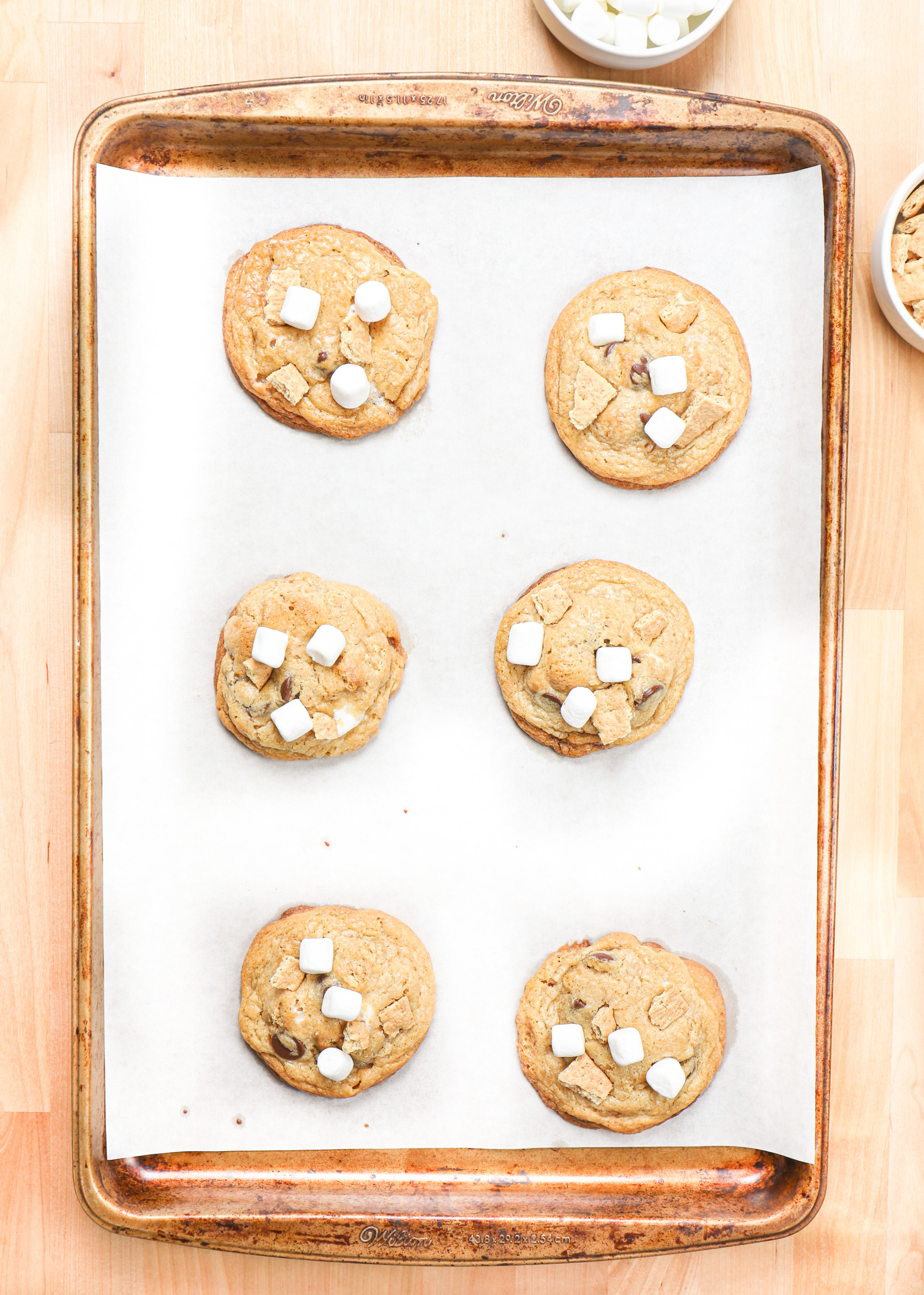 Overhead view of a batch of smores cookies halfway through baking time getting additional toppings added.