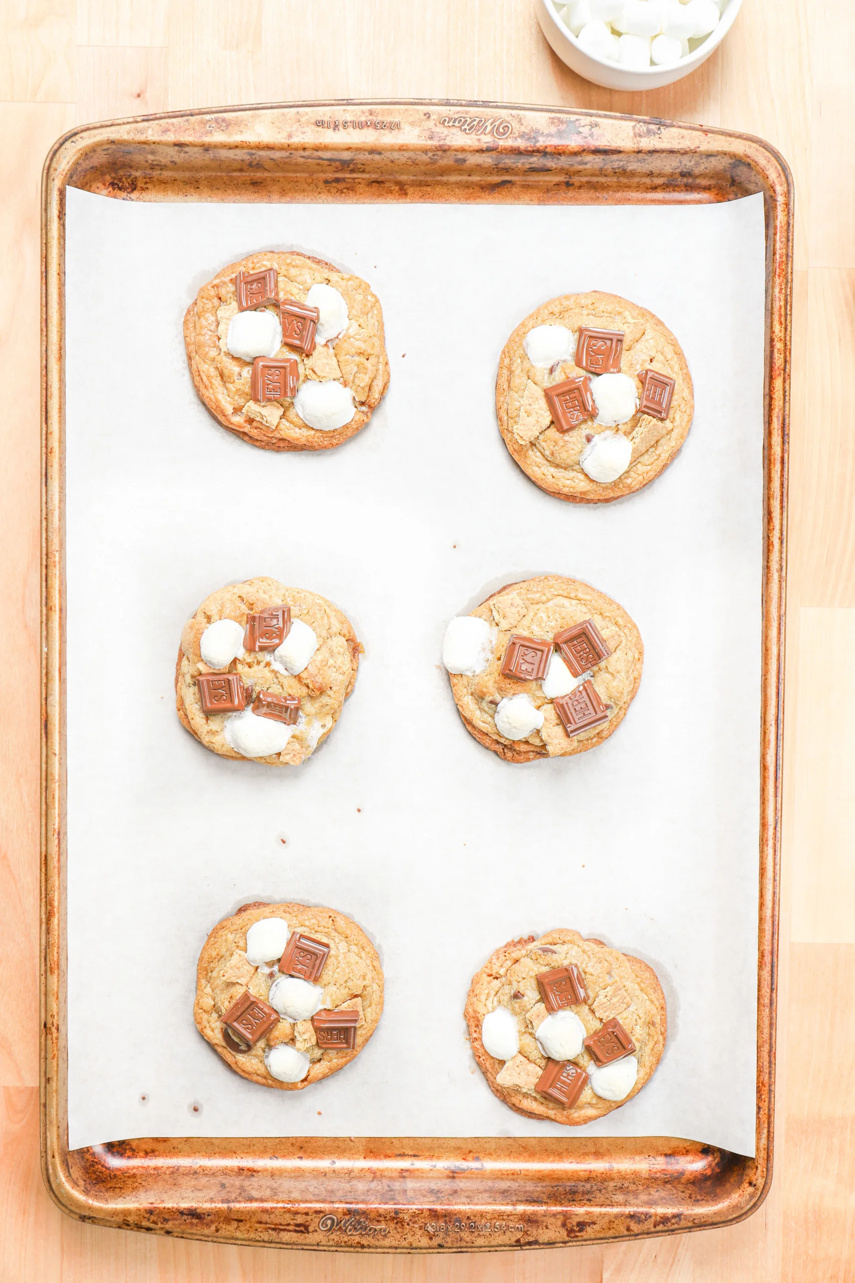 Overhead view of a batch of smores cookies right out of the oven on a parchment paper lined baking sheet.