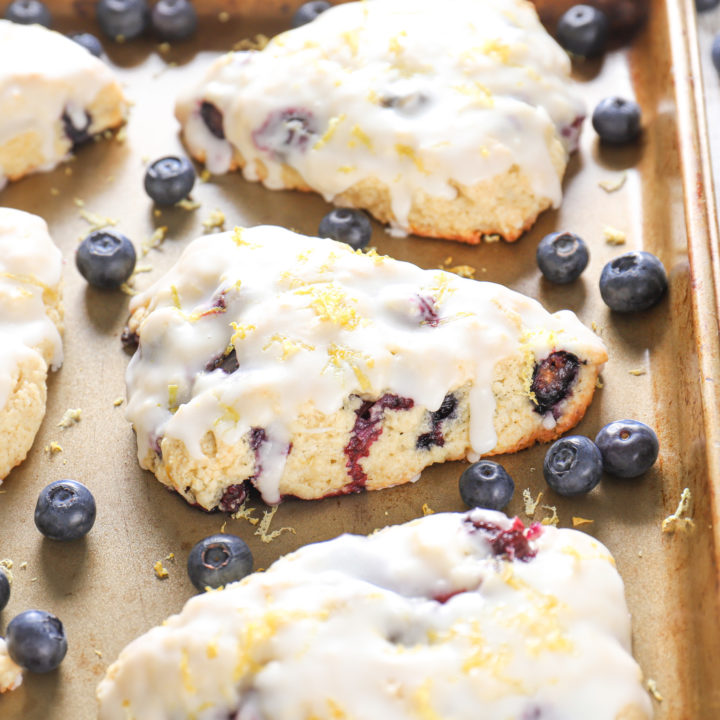 Side view of a lemon blueberry scone on an aluminum baking sheet surrounded by other scones.