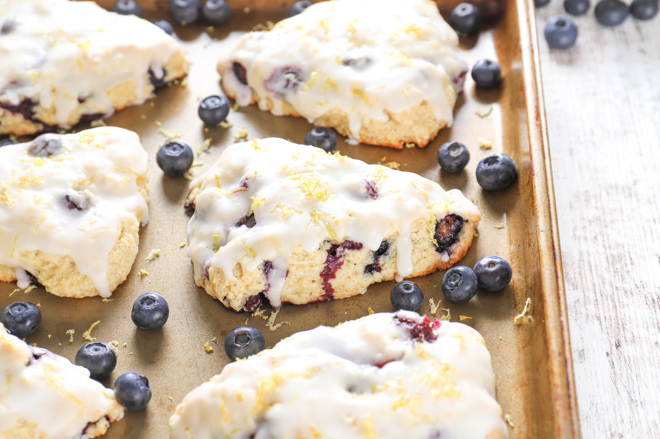 Side view of a lemon blueberry scone on an aluminum baking sheet surrounded by other scones.