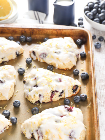 Side view of a lemon blueberry scone on an aluminum baking sheet surrounded by additional scones.