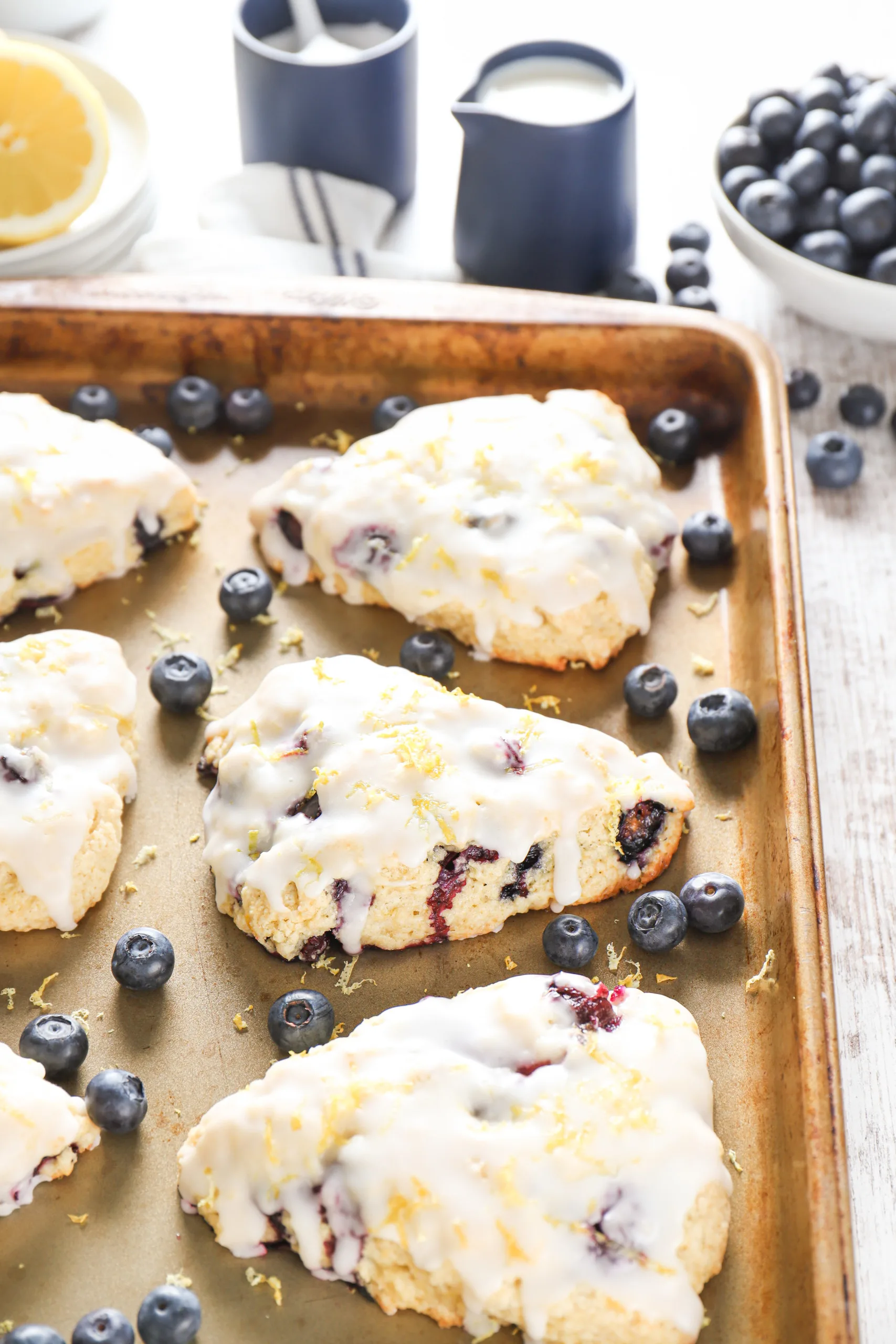 Side view of a lemon blueberry scone on an aluminum baking sheet surrounded by additional scones.