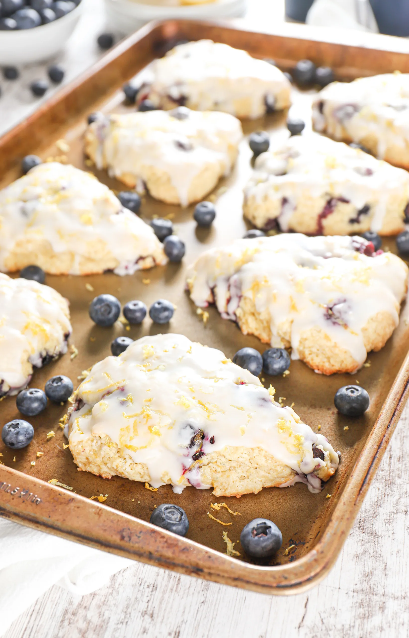 Side angle view of a batch of blueberry lemon scones on an aluminum baking sheet.