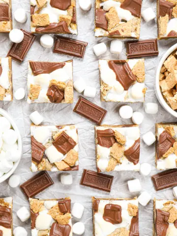 Overhead view of a batch of peanut butter smores bars on a piece of parchment paper surrounded by chocolate pieces and mini marshmallows.