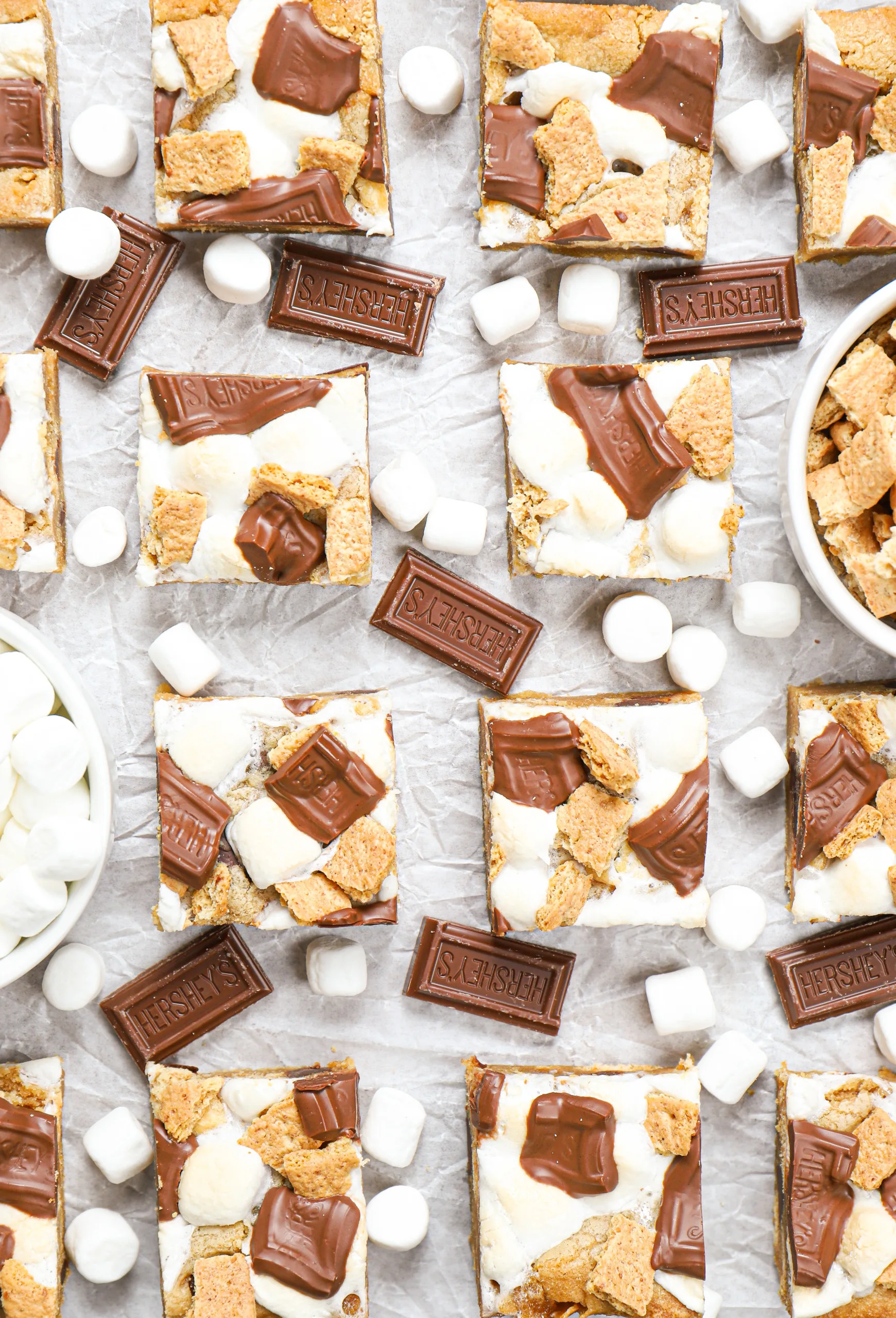Overhead view of a batch of peanut butter smores bars on a piece of parchment paper surrounded by chocolate pieces and mini marshmallows.