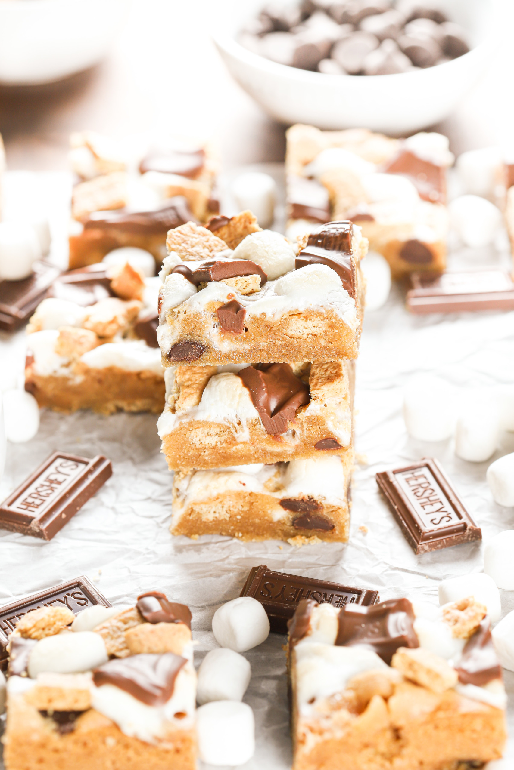Side view of three peanut butter smores bars on a piece of parchment paper surrounded by the remaining bars.