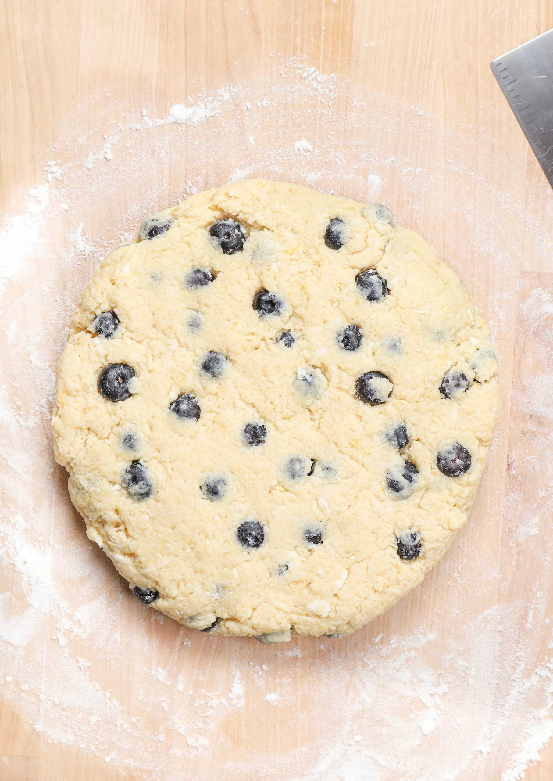 Overhead view of the lemon blueberry scone dough in a circle on a butcher block countertop.