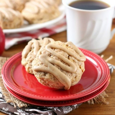 Two apple cider scones on a small red plate with a cup of coffee and a plate of scones in the background.