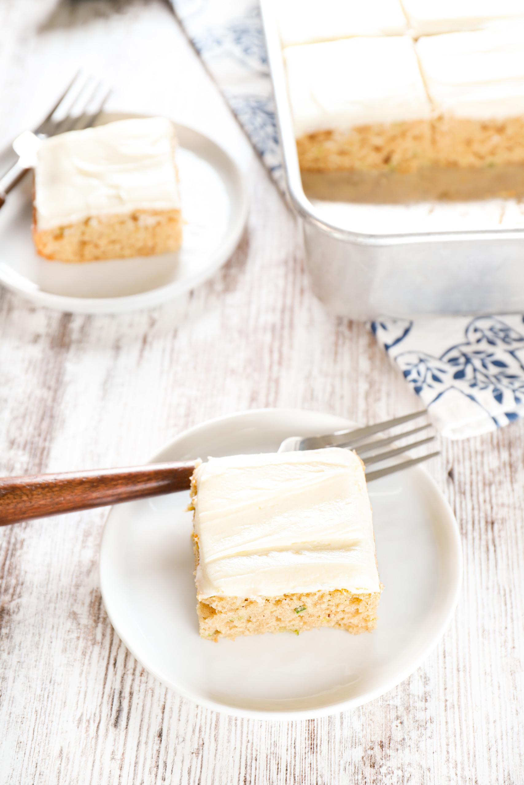 Side view of two zucchini bars on small white plates with the remaining bars in the pan in the background.