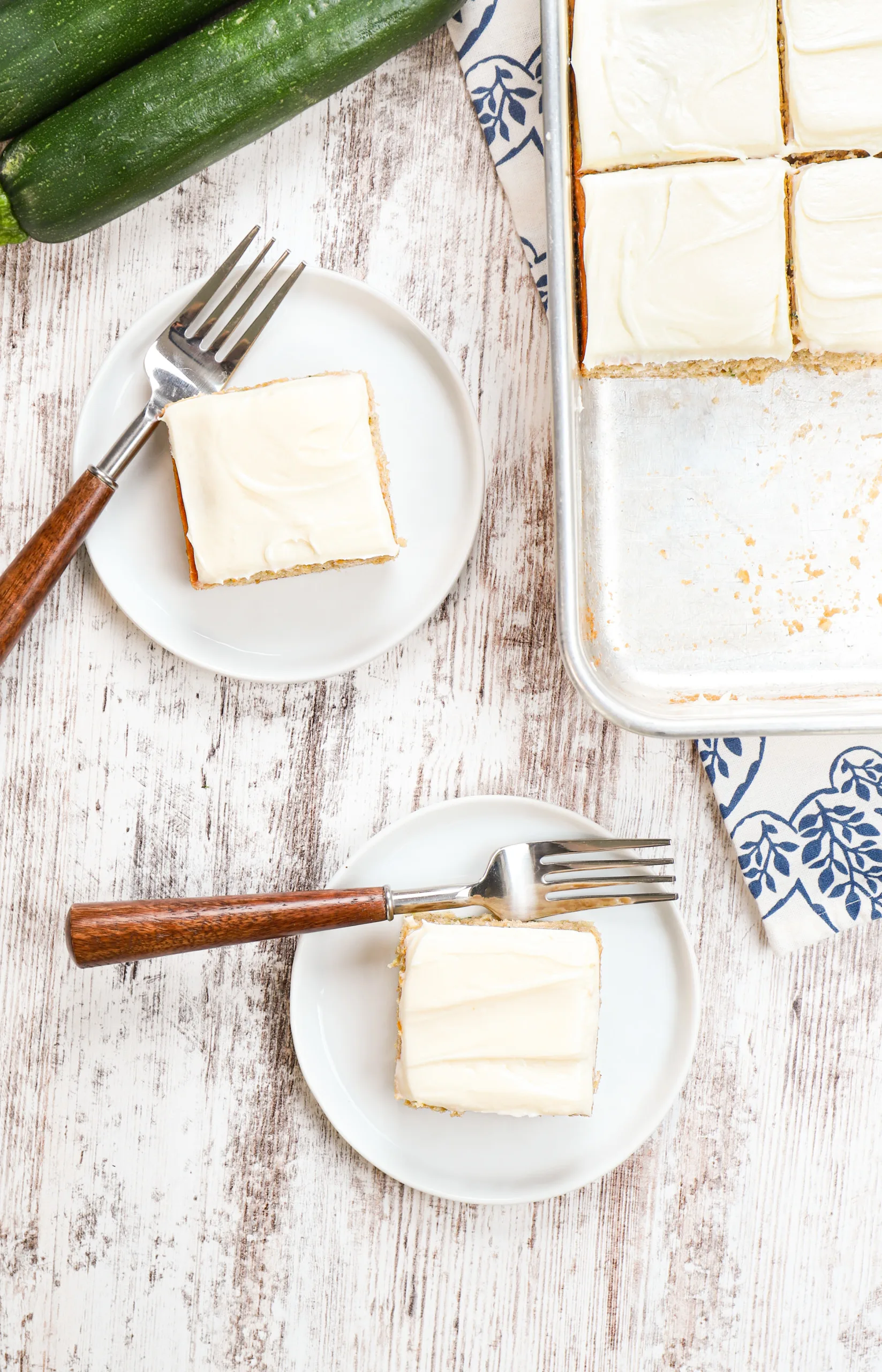 Overhead view of zucchini bars on small white plates and the remaining pan of bars on a white wooden board.