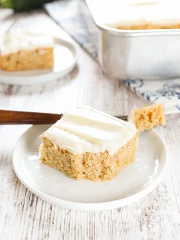 Up close view of a zucchini bar on a small white plate with a fork that has a bite on it.