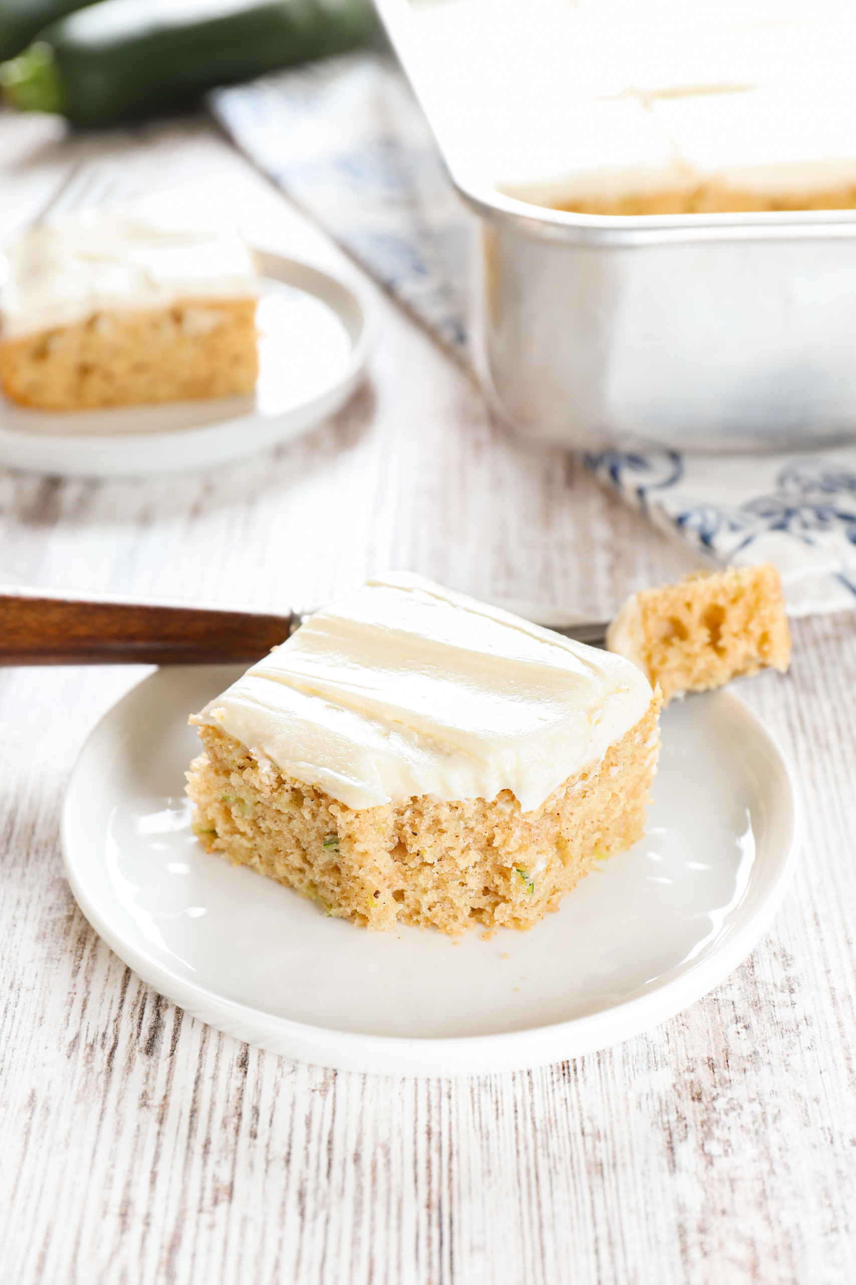 Up close view of a zucchini bar on a small white plate with a fork that has a bite on it.