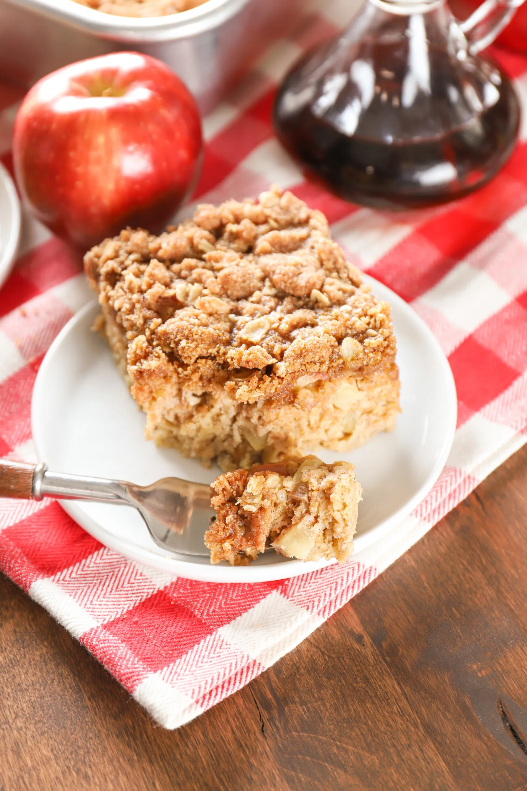 A piece of apple streusel baked oatmeal on a small white plate with a bite of oatmeal on the fork.
