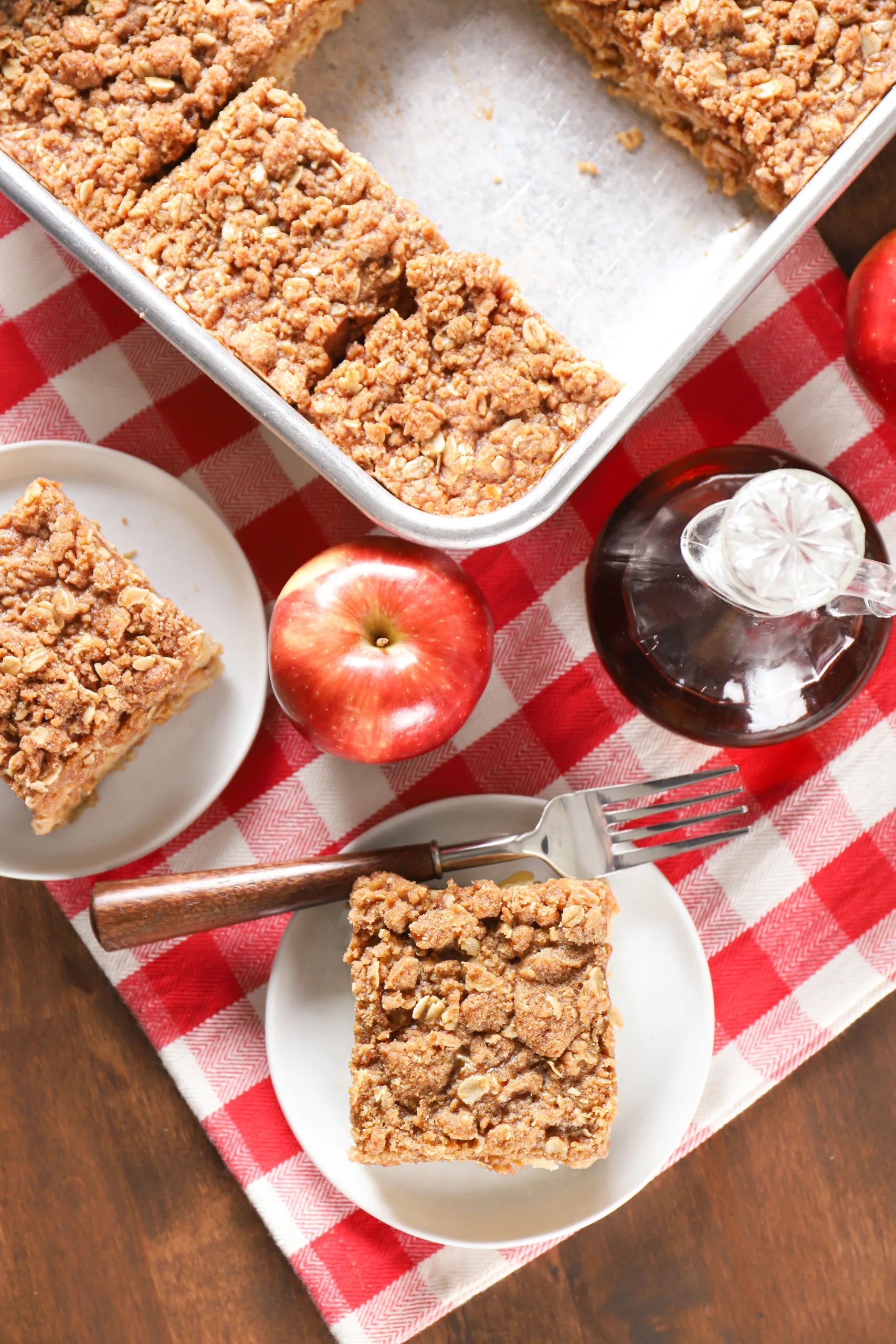 Overhead view of a two white plates with a piece of apple streusel baked oatmeal and the pan with the remaining baked oatmeal behind them.